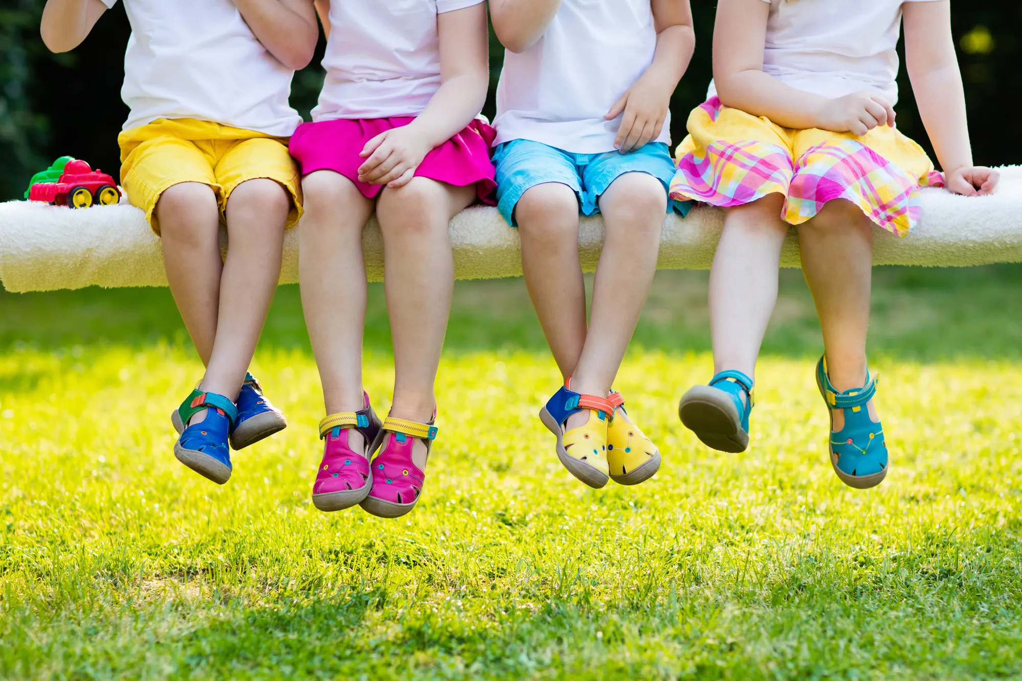 Vier Kinder sitzen mit bunten Sommerschuhen auf einer Schaukelbank